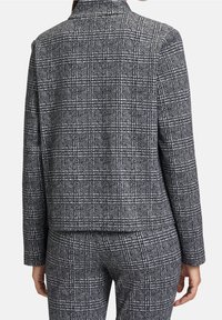Blazer a quadri grigio e nero con colletto, design strutturato e maniche lunghe. I tessuti presentano una trama testurizzata con chiari motivi a griglia.