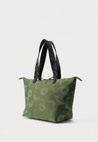 Zaļa iepirkumu soma ar lielu ziedu rakstu un melnām rokturiem, ar rāvējslēdzēja aizdari, attēlota uz vienkārša balta fona.