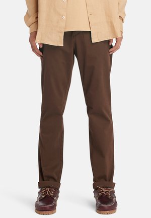 Brown cotton chinos with a straight cut and subtle sheen, paired with dark burgundy lace-up shoes featuring a textured sole.