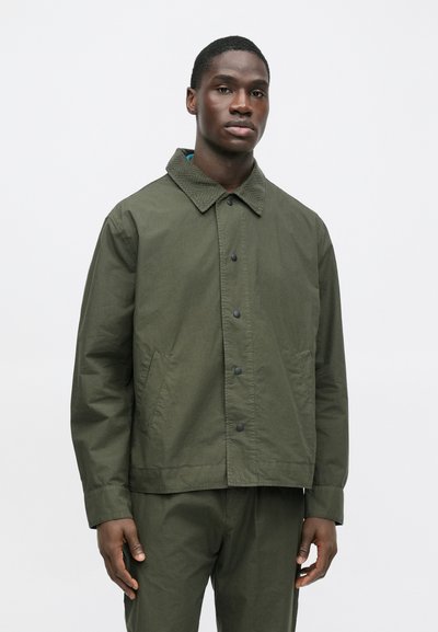 Olivovo zelená bunda s výrazným golierom, zapínaním na gombíky vpredu a bočnými vreckami. Vyrobená z textúrovaného, ľahkého materiálu.