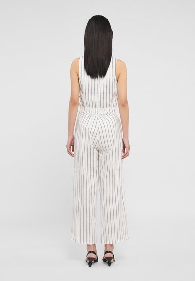 Jumpsuit à rayures blanches avec des jambes larges et une taille cintrée, présentant de fines lignes verticales noires. Tissu lisse, design sans manches.