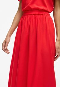 Jupe rouge fluide en tissu léger, dotée d'une taille élastique et d'une texture douce, descendant en plis délicats.