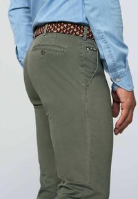 Olivgrüne Hose mit schlankem Schnitt und subtiler Textur, ausgestattet mit einem gewebten, mehrfarbigen Gürtel und einer Gesäßtasche mit Knopfdetail.