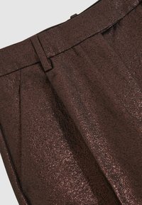 Kiiltävät, kohokuvioidut ruskeat housut, joissa on laskostettu etuosa, räätälöity vyötärö ja hienovarainen metallinen hohde koko kankaan pinnalla.