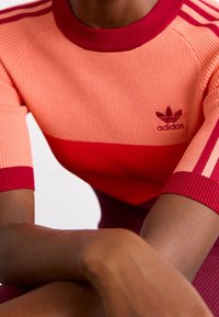 Röd och rosa ribbad stickad Adidas-tröja med korta ärmar, med logotyp på bröstet och tre ränder på axlarna.