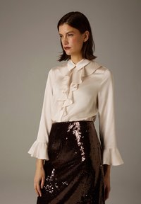 Cream blouse with ruffled front and collar, long sleeves with flared cuffs; paired with a dark sequin pencil skirt featuring a glossy texture.