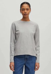 Grijze langmouw t-shirt gemaakt van zachte stof, met een ronde halslijn en een relaxed fit, gecombineerd met blauwe jeans.