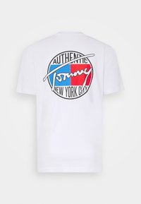 Bílý tričko s velkým kulatým logem na zádech, které obsahuje modré a červené bloky a text "Autentický Tommy New York City".