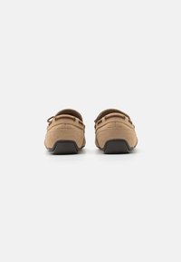 Tan casual shoes with a textured upper, two eyelets, and a brown rubber sole. The back features a slight rise with a rounded shape.