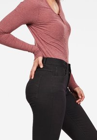Musta, tiukka farkut korkealla vyötäröllä ja sileällä pinnalla, jossa on takataskut ja hienot ompeluyksityiskohdat. Yhdistetty ribbikuvioiseen mauve-paitaan.
