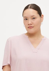 Ροζ κοντομάνικο μπλουζάκι με V λαιμόκοψη και διακριτές ραφές. Φτιαγμένο από ένα λείο, ελαφρύ ύφασμα, προσφέροντας χαλαρή εφαρμογή.