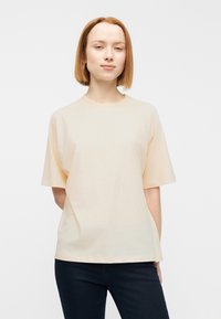 Κοντομάνικο μπλουζάκι σε απαλό ροδακινί χρώμα από μαλακό ύφασμα. Χαλαρή εφαρμογή με στρογγυλή λαιμόκοψη και χωρίς ορατά σχέδια ή μοτίβα.