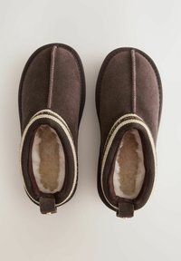 Pruunist nahast sussid, millel on lambanaha vooder, tekstureeritud ülemine osa, keskmine õmblus ja dekoratiivsed punutud detailid avas.