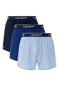 Trois paires de boxers pour hommes : bleu foncé uni, bleu marine uni et rayé bleu et blanc. Comprend une taille élastique avec le logo "Lacoste".