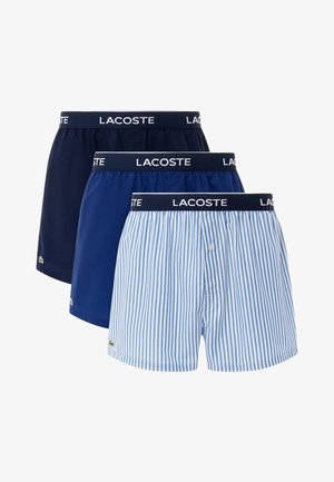 Három pár férfi boxer: egyszínű sötétkék, egyszínű tengerészkék és kék-fehér csíkos. Rugalmas derékpánt jellemzi, amelyen a "Lacoste" márkaneve szerepel.