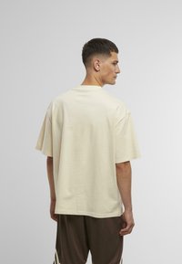 T-shirt surdimensionnée couleur crème en tissu doux, avec un col rond et des manches courtes. Design épuré, sans motifs ni quincaillerie visible.