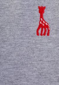 Giraffa ricamata rossa con macchie bianche su uno sfondo di tessuto grigio chiaro.