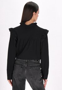 Maglietta nera cropped con maniche lunghe, spalle arricciate e colletto alto. Abbinata a jeans neri sbiaditi a vita alta.