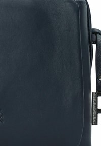 Navy Leder Umhängetasche mit glatter Textur, abgerundeten Kanten und silbernem Beschlag mit einem Verschluss. Markenlogo auf der Vorderseite eingeprägt.