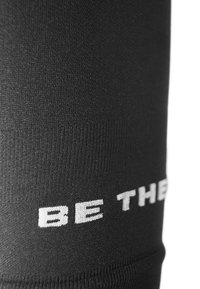 Schwarze sportliche Leggings aus strukturiertem Stoff, mit enganliegendem Design und weißem Text "BE THE" entlang des unteren Randes.