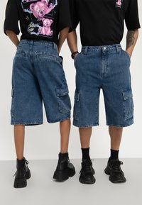 Pantalones cortos de mezclilla cargo, de longitud media, en lavado azul oscuro. Cuenta con dos bolsillos laterales tipo cargo, costuras en contraste y un ajuste relajado.