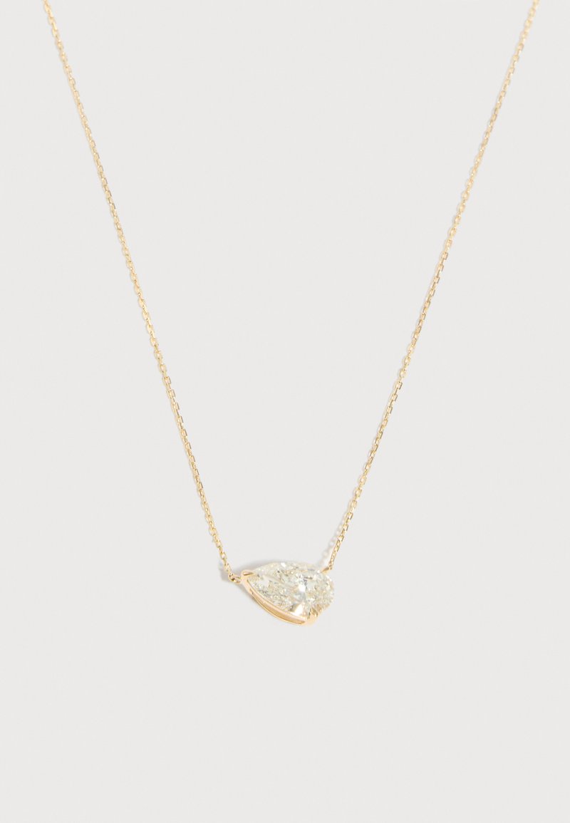 Λεπτό χρυσό κολιέ με αλυσίδα και ένα μόνο διαμάντι σε σχήμα αχλαδιού, διαυγές, τοποθετημένο στο κέντρο πάνω σε απλό ανοιχτό φόντο.