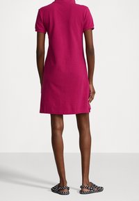 Vestido de polo fucsia con corte recto, mangas cortas, aberturas laterales y textura suave. Combinado con sandalias de patrón en blanco y negro.