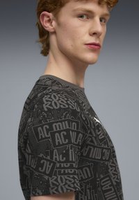 Sort bomuld t-shirt med et grafisk tryk af forskellige logoer i grå nuancer. Rund hals og korte ærmer.