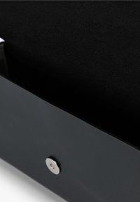 Bolso de cuero negro con un diseño elegante, que cuenta con un cierre a presión plateado en un interior texturizado, mostrando un estilo y una estructura minimalistas.