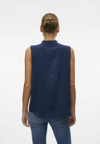 Haut sans manches bleu marine avec une finition texturée, coupe décontractée et col montant. Associé à un jean bleu clair avec poches arrière.