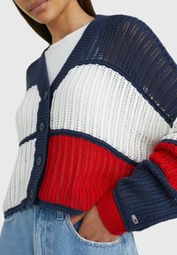 Cardigan a maglia con motivi a blocchi in blu navy, rosso e bianco, chiusura con bottoni e polsini a coste con dettaglio del logo. Design a trama aperta e testurizzata.