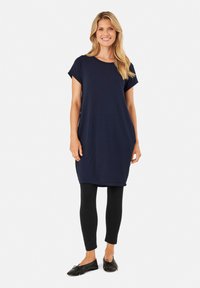 Marinblå knälång klänning med korta ärmar, mjukt tyg, avslappnad passform, kombinerad med svarta leggings och svarta platta skor.