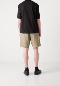 Musta puuvillainen t-paita, lyhyet hihat, rento istuvuus; beiget shortsit, sileä pinta, polven alle ulottuvat. Mustat matalakärkiset lenkkarit.