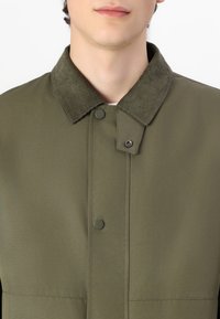 Olive green jacket featuring a corduroy collar, snap buttons, and a smooth texture, designed with a minimalist front closure.