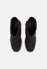 Czarne botki za kostkę z gładką cholewką z tkaniny, bocznymi zamek błyskawicznymi oraz kontrastującymi brązowymi gumowymi podeszwami. Wnętrze w feature'm nazwę marki "ANNA FIELD."