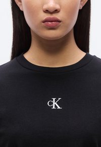 Μαύρο βαμβακερό μπλουζάκι με στρογγυλή λαιμόκοψη και λευκό λογότυπο "cK" τυπωμένο στο στήθος. Ομαλή υφή, casual σχεδιασμός.