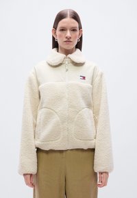 Μπλούζα με φερμουάρ σε κρεμ χρώμα, με σώμα από υφασμάτινο φλις με υφή, λεία επάνω περιοχή, μεγάλες πλαϊνές τσέπες και λαιμόκοψη με γιακά.