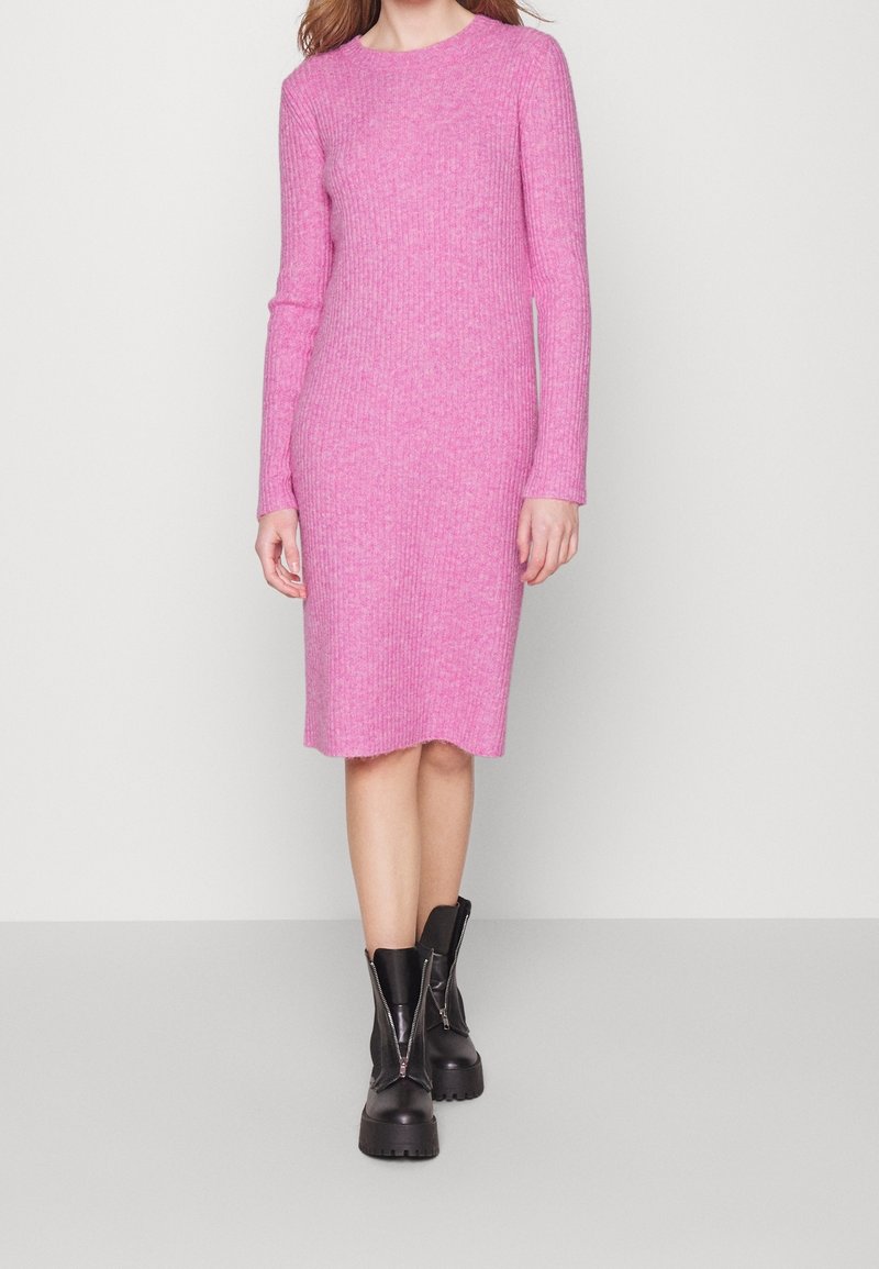 Rosa ribbad stickad klänning med långa ärmar och rundad halsringning. Har en lätt ojämn nederkant. Matchas med svarta kraftiga stövlar.