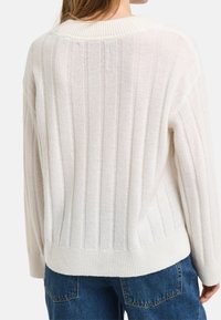 Pull blanc côtelé à col rond, tricot texturé, coupe légèrement courte, associé à un jean bleu foncé.