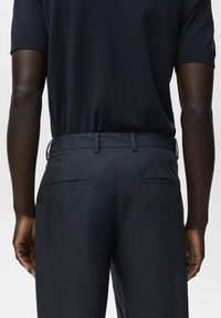Marineblauw polo met korte mouwen, gecombineerd met donkere broek met een platte voorkant en twee achterzakken, gladde textuur, slim fit.