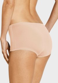 Persikofärgade högmidjade trosor med en slät textur, sömlös design och mjukt tyg, som erbjuder full täckning och en ren silhuett.