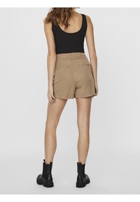 Shorts beiges taille haute avec poches arrière, complétés par un haut sans manches noir et des bottines noires. Texture de tissu lisse.
