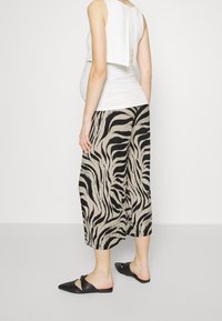 Svart- och beige randiga plisserade culotter i kombination med en vit topp. Modellen bär svarta tofflor, vilket ger en avslappnad men ändå strömlinjeformad look.