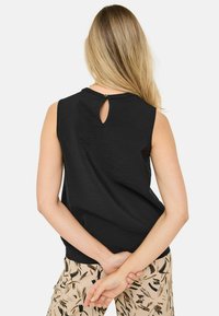 Černý top bez rukávů z texturované látky s knoflíkovým detaily ve tvaru klíčové dírky na zadní straně a volným střihem. V kombinaci s vzorovanými kalhotami.