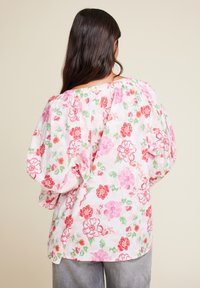 Blomstrete bluse med pufferm, med en hvit bakgrunn prydet med røde og rosa blomster og grønne detaljer. Lett stoff, løs passform.