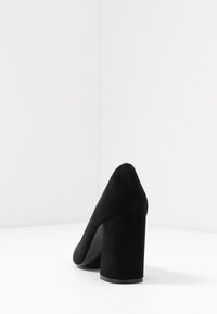 Black high-heeled shoe made of suede, featuring a pointed toe and a wide block heel. The sole is slightly visible, with a smooth finish.
