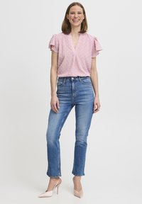 Blusa rosa chiaro a V con maniche corte a volant e pois bianchi, abbinata a jeans blu a vita alta e tacchi rosa pallido.
