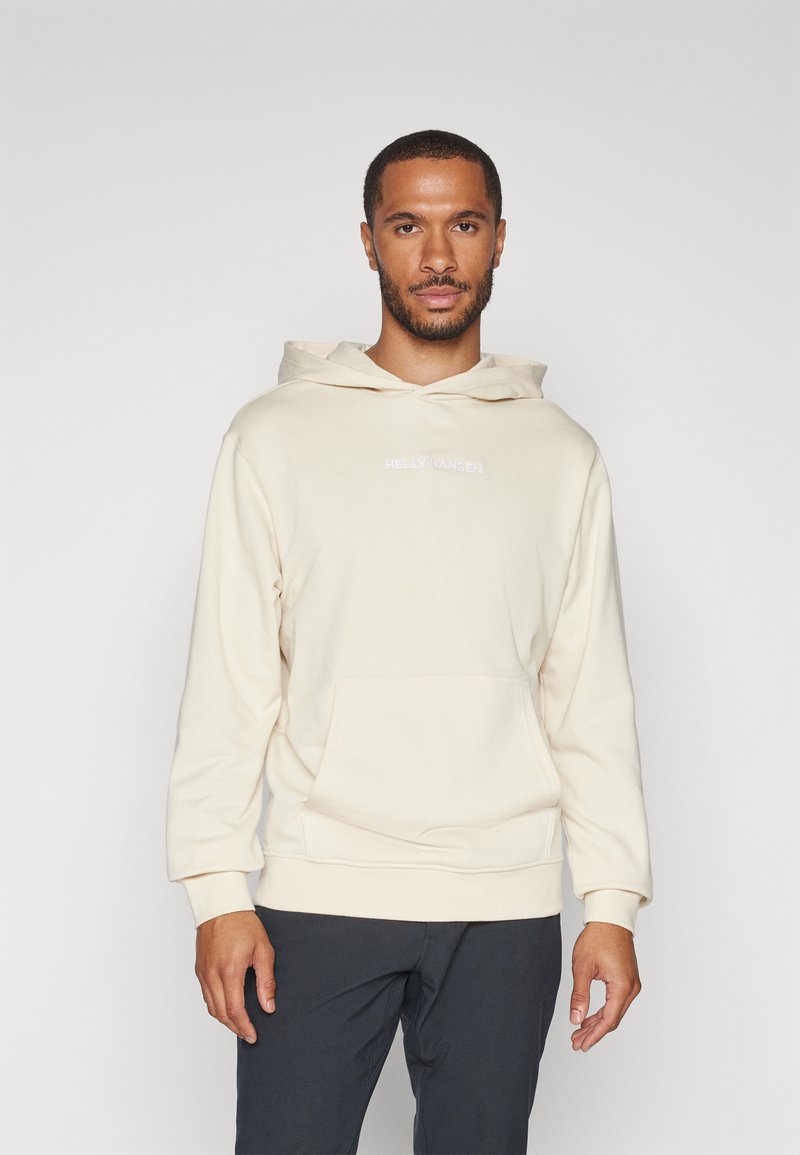 Kremowy hoodie z kieszenią z przodu, kapturem ze sznurkiem oraz logo "HELly HANSEN". Dopasowane mankiety i miękka, gładka struktura.
