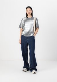 Striped short-sleeve t-shirt in cream and navy, paired with wide-leg dark denim jeans. Model carries a beige shoulder bag and wears sneakers.