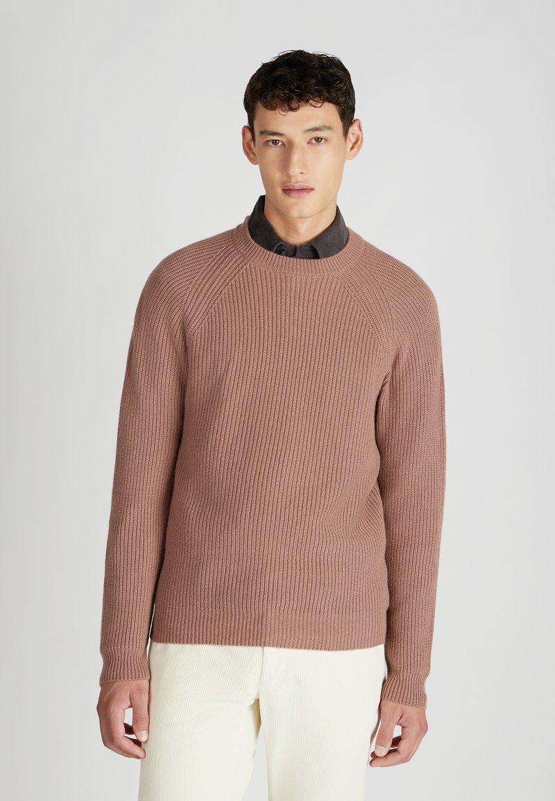 Mauvefarbener, gerippter Strickpullover mit Raglanärmeln und Rundhalsausschnitt, über einem dunklen Hemd mit Kragen getragen; hat eine strukturierte Oberfläche.